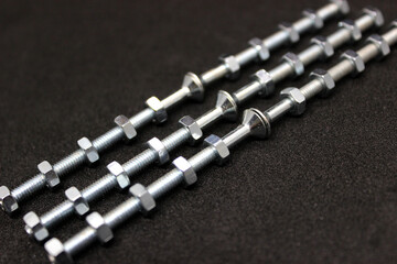 Shiny Iron Bolts With Nuts Screwed On Them Lie In Even Rows Isolated On Black Surface
