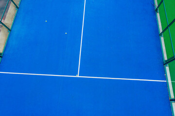 aerial drone bird's-eye view of a blue paddle tennis court with balls on its surface
