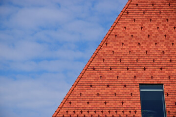 steep red clay tile sloped roof. bright blue sky wand white clouds. roof window or skylight. metal...