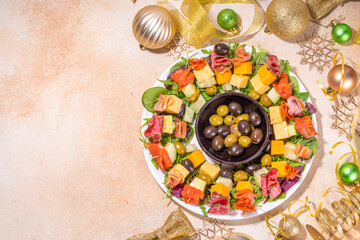 Christmas party dinner, trendy layout appetizers. Charcuterie wreath made from sausage, meat, cheese, olives, greens on beige table background with gold Christmas decor top view copy space