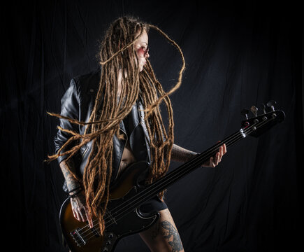 Woman Musician Playing The Bass Guitar. Tattoos And Dreadlocks