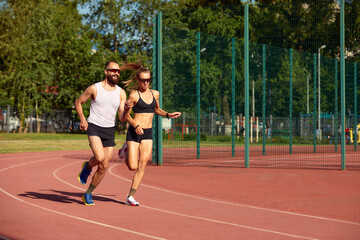 Young family promoting healthy lifestyle. Woman and man run stadium. Coach and sportsman motion run training before race. Couple runners training outdoors. Couple or family live healthy lifestyle.