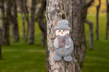 Homemade snowman made of gray fabric hangs on a coniferous tree in the forest, Christmas decoration for the holiday