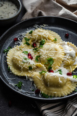 Mezzelune filled with parmesan and asparagus with creamy sauce decorated with parsley and pomegranate seeds on dark plate.