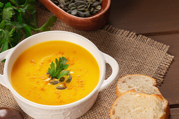 Pumpkin soup and parsley on rustic wooden table. Seasonal autumn food - Spicy pumpkin ans carrot soup