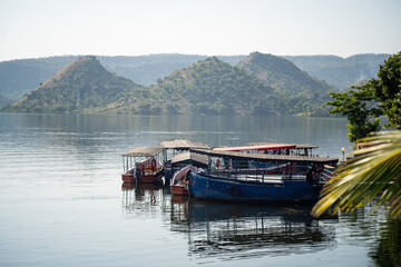 boats moored tied on Dhebar lake with Aravalli hills in the distance at dusk showing the beautiful view of asia's largest manmade lake and popular tourist and holiday destination