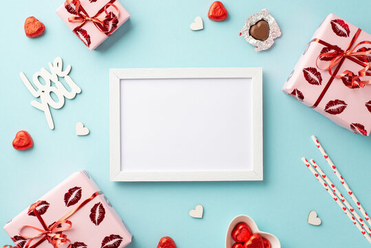 Valentine's Day concept. Top view photo of photo frame gift boxes in wrapping paper with kiss lips pattern heart shaped candies straws inscription love on isolated light blue background with copyspace
