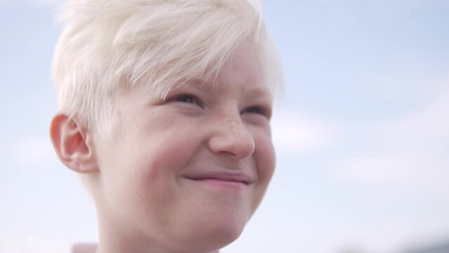 Close-up of the face, a happy blond boy against the sky.