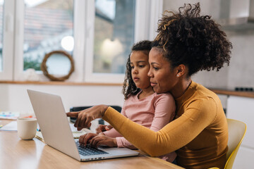 Mom teaches her little girl how to use laptop