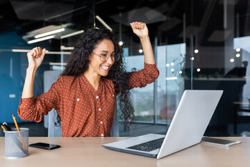 A beautiful young Latin American woman freelancer sits in the office at the table with a laptop,...