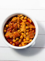  Top view of a casserole of tripe with chickpeas on a white wooden background. Winter comfort food. (Callos a la madrileña)