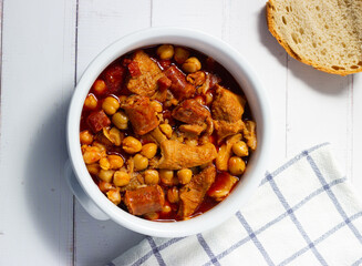  Top view of a casserole of tripe with chickpeas on a white wooden background. Winter comfort food. (Callos a la madrileña)