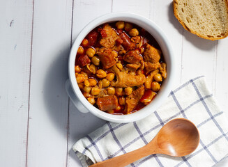  Top view of a casserole of tripe with chickpeas on a white wooden background whith rustic spoon. Winter comfort food. (Callos a la madrileña)