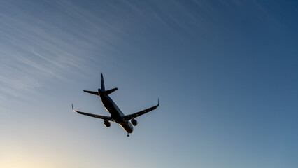 The silhouette of a passenger plane coming in for landing against the backdrop of the sunset sky.