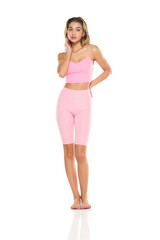 Naklejka premium a young barefeet woman in pink short leggings and top posing on a white studio background