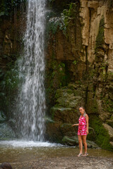 one girl in a pink dress stands at a waterfall