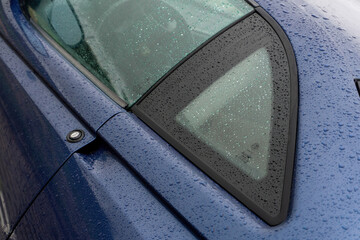 The body of a blue car covered with raindrops