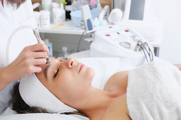 The cosmetologist makes the procedure Microdermabrasion of the skin of the face of a beautiful, young woman in a beauty salon. Cosmetology and professional skin care.