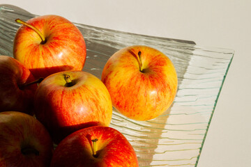 A set of apples on a transparent dish. Apples are yellow-red. Hard light.