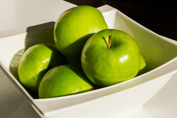 A set of green apples in a bowl. Close-up. Green apples. Hard light. Shadow.