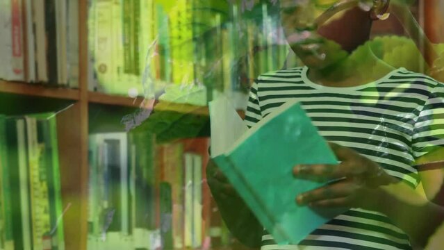 Animation of leaves over african american schoolgirl reading book