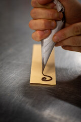 Baker hands Writing Celebratory Message Using Chocolate Icing Ganache Piped from Icing Bag