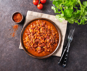 Stewed oxtails with vegetables in a wooden plate on a dark background with fresh tomatoes and herbs. Meat stew. The concept of traditional Spanish cuisine.