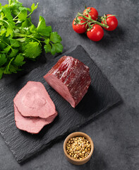 Juicy baked roast beef on a slate board with tomatoes and fresh herbs on a dark  background.