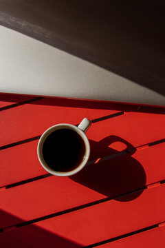 A cup of coffee and a laptop on a red table. Kind of light. Hard light, shadows, top view.