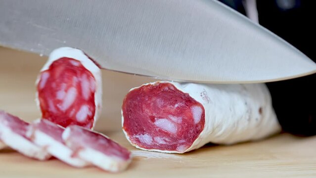 Traditional Spanish Fuet thin dried sausage. Closeup of cutting sausage fuet from pork meat on a table at a kitchen. Slices of red Spanish dry sausage fuet