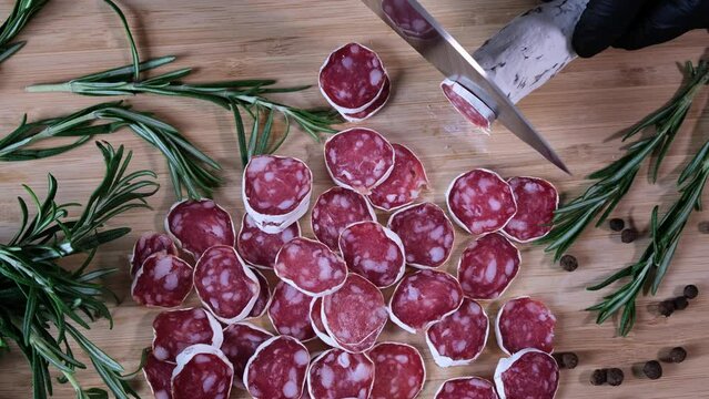 Traditional Spanish Fuet thin dried sausage. Closeup of cutting sausage fuet from pork meat on a table at a kitchen. Slices of red Spanish dry sausage fuet