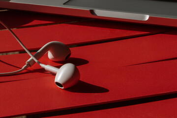 Laptop and headphones on a red table. Hard light, shadows. Close-up.