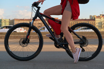 Beautiful slender, long, female legs on a black bicycle. Young girl loves to ride a bike.