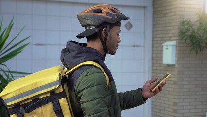 Food delivery concept. Young African American driver with backpack looking smart phone to deliver products for customers who order online purchases. Black male smiling happy with his job. - Powered by Adobe