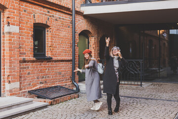 Two girls walking on street together and holding their hands. They are wearing spring or autumn clothes and they are happy. Friendship and relationship concept