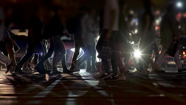 Crowd of unrecognizable people walking on busy city crosswalk during evening rush hour. Pedestrians walking on the crosswalk. Unrecognizable people on city zebra crossing street at night. Slow motion