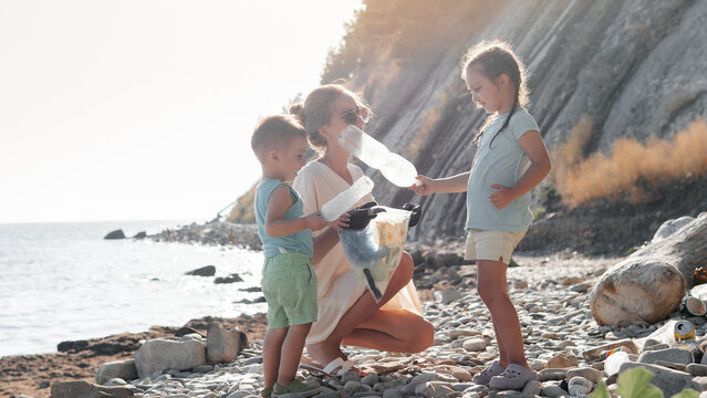 Little siblings helping mother to collect garbage on sea beach in plastic bag. Happy family activists collecting trash. Concept about environmental conservation pollution problems and responsibility.