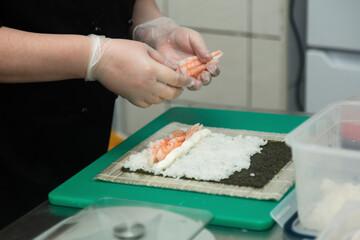 female chef makes rolls with rice and nori in the restaurant kitchen