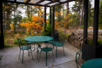 Open gazebo with a round table and chairs against the backdrop of an autumn forest