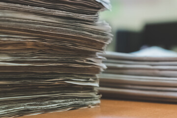 Detail of a stack of newspapers in the foreground. In the background a smaller pile of out-of-focus...