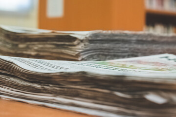 Close up of two stacks of newspapers, placed one in front of the other. Defocused library room...