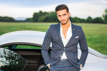 Young attractive man in business suit leaning on his new car
