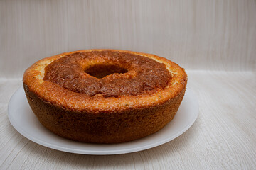 A freshly baked homemade round cake with a hole in the center on a dish isolated on light background and empty space for text. Traditional Portuguese yogurt cake