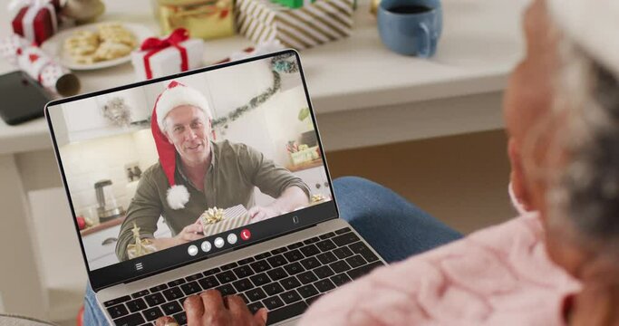 Senior african american woman with santa hat having laptop video call with happy caucasian man