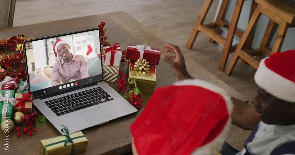 Wall mural Diverse couple with santa hats having laptop video call with happy african american man