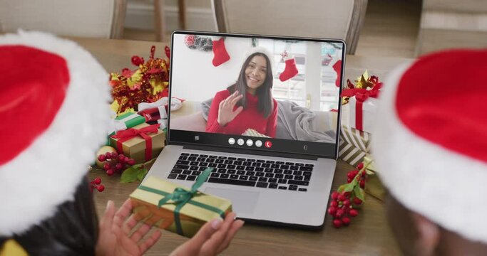 Diverse couple with santa hats having laptop video call with happy biracial woman