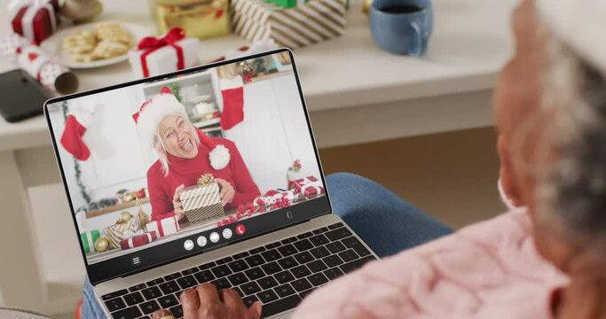 African american woman with santa hat having laptop video call with happy caucasian woman
