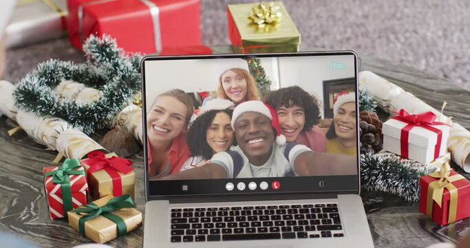 Diverse couple with santa hats having laptop video call with diverse friends