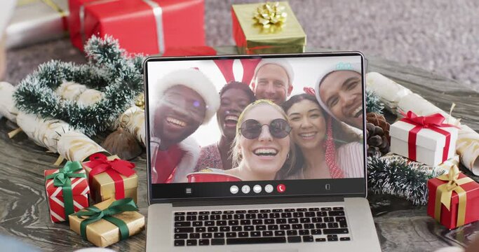 Diverse couple with santa hats having laptop video call with diverse friends