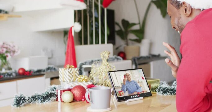 Animation of african american man in santa hat on tablet video call with man at christmas